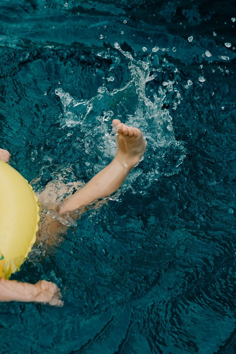 Child's legs splashing in blue water with yellow float.